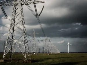 Hoogspanningsmasten in Nederlands polderland onder dreigende stormwolken, met een windturbine op de achtergrond.